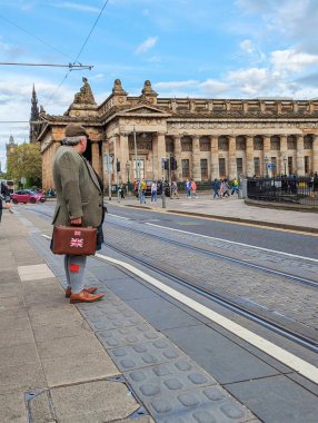 Edinburgh, İskoçya, 10 Mayıs 2024: Geleneksel İskoç etek ve spor üniformaları giyen bir İskoç Prenses Caddesi 'nde bir tramvay bekliyor..