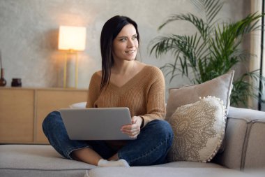 Dizüstü bilgisayar kullanan gülümseyen bir kadın, evdeki koltukta oturuyor, güzel bir bayan alışveriş yapıyor ya da sosyal ağda sohbet ediyor, eğleniyor, film izliyor, bilgisayar projesinde serbest çalışıyor.
