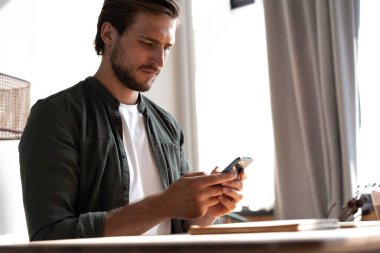 İş yerindeki genç çalışan cep telefonu kullanıyor, akıllı telefondan sosyal medyayı kontrol ediyor, ara veriyor, boşluk kopyalıyor