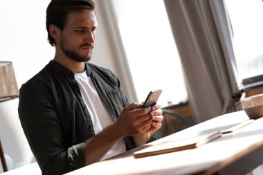 İş yerindeki genç çalışan cep telefonu kullanıyor, akıllı telefondan sosyal medyayı kontrol ediyor, ara veriyor, boşluk kopyalıyor