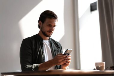 İş yerindeki genç çalışan cep telefonu kullanıyor, akıllı telefondan sosyal medyayı kontrol ediyor, ara veriyor, boşluk kopyalıyor