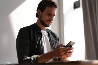 İş yerindeki genç çalışan cep telefonu kullanıyor, akıllı telefondan sosyal medyayı kontrol ediyor, ara veriyor, boşluk kopyalıyor