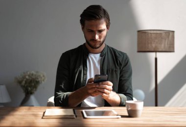 İş yerindeki genç çalışan cep telefonu kullanıyor, akıllı telefondan sosyal medyayı kontrol ediyor, ara veriyor, boşluk kopyalıyor