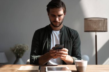 İş yerindeki genç çalışan cep telefonu kullanıyor, akıllı telefondan sosyal medyayı kontrol ediyor, ara veriyor, boşluk kopyalıyor