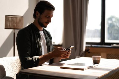 İş yerindeki genç çalışan cep telefonu kullanıyor, akıllı telefondan sosyal medyayı kontrol ediyor, ara veriyor, boşluk kopyalıyor