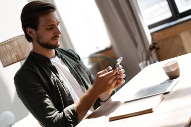 İş yerindeki genç çalışan cep telefonu kullanıyor, akıllı telefondan sosyal medyayı kontrol ediyor, ara veriyor, boşluk kopyalıyor