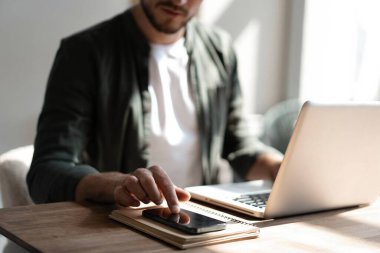 İş yerindeki genç çalışan cep telefonu kullanıyor, akıllı telefondan sosyal medyayı kontrol ediyor, ara veriyor, boşluk kopyalıyor