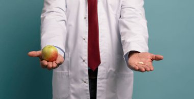 Elma ve hap taşıyan beyaz önlüklü yakışıklı olgun bir doktorun portresi.