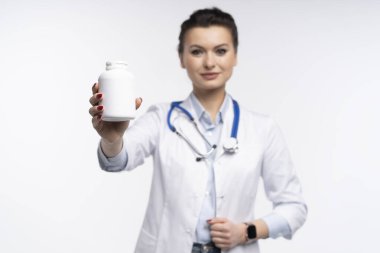 Çekici, çekici bir kadın uzman terapistin fotoğrafı beyaz arka planda beyaz doktor cübbesi giyerek el ele tutuşan haplar.