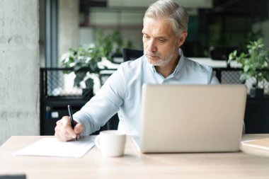 Gülümseyen 40 'lı yılların erkek muhasebeci analisti elinde belgeler, dizüstü bilgisayarda çalışıyor online ticaret pazarı teknolojisi araştırmaları yapıyor. Ofisinde evrak işleriyle uğraşan odaklanmış bir işadamı.