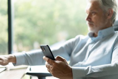 Orta yaşlı iş adamı elinde akıllı telefon tutarak çalışıyor. Olgun 45 yaşındaki işadamı yöneticisi, iş sahibi veya girişimci cep telefonu kullanarak masada oturuyor.