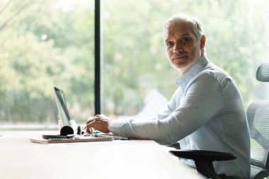 Mutlu Avrupalı iş adamı CEO 'su bilgisayar kullanıyor, daktilo kullanıyor, modern ofiste çalışıyor, çevrimiçi veri pazarı analizi yapıyor, bilgisayar kopyalama alanı olan dizüstü bilgisayara bakarak teknoloji stratejisi planlıyor.