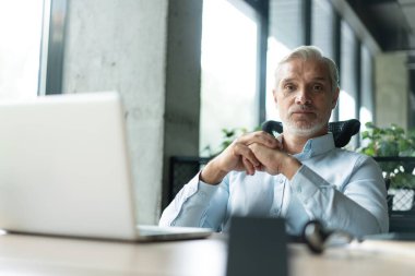 İş yerinde bilgisayar kullanarak kameraya bakan olgun iş adamı. Gülümseyen erkek şirket çalışanı, proje yöneticisi veya girişimci portresi
