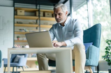 Gülümseyen işadamı ofis lobisinde oturmuş dizüstü bilgisayarla çalışıyor. Ofis lobisinde çalışan bir erkek işadamı..