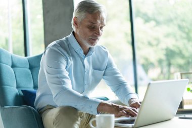 Gülümseyen işadamı ofis lobisinde oturmuş dizüstü bilgisayarla çalışıyor. Ofis lobisinde çalışan bir erkek işadamı..
