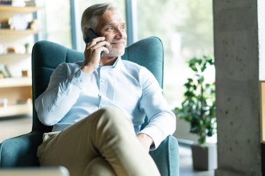 Akıllı telefonlu bir iş adamı ofisinden cep telefonuyla arıyor. Beyaz adam ofis lobisinde oturuyor. Arama yapmak için cep telefonu kullanıyor.