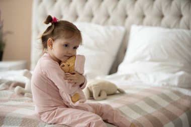 Pijama giymiş sevimli küçük bir kız evde oyuncak tavşanına sarılıyor, mutlu çocukluk konsepti, kapalı alanda.