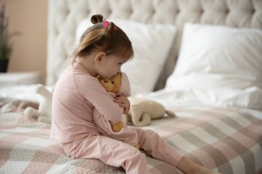 Pijama giymiş sevimli küçük bir kız evde oyuncak tavşanına sarılıyor, mutlu çocukluk konsepti, kapalı alanda.