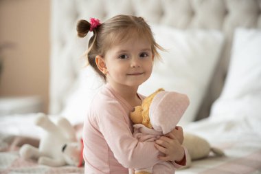 Pijama giymiş sevimli küçük bir kız evde oyuncak tavşanına sarılıyor, mutlu çocukluk konsepti, kapalı alanda.