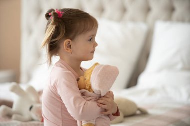 Pijama giymiş sevimli küçük bir kız evde oyuncak tavşanına sarılıyor, mutlu çocukluk konsepti, kapalı alanda.