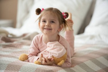 Pijama giymiş sevimli küçük bir kız evde oyuncak tavşanına sarılıyor, mutlu çocukluk konsepti, kapalı alanda.