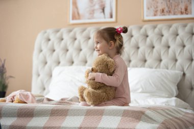 Pijama giymiş sevimli küçük bir kız evde oyuncak tavşanına sarılıyor, mutlu çocukluk konsepti, kapalı alanda.