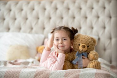 Pijama giymiş sevimli küçük bir kız evde oyuncak tavşanına sarılıyor, mutlu çocukluk konsepti, kapalı alanda.