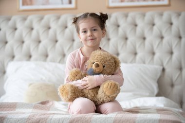 Pijama giymiş sevimli küçük bir kız evde oyuncak tavşanına sarılıyor, mutlu çocukluk konsepti, kapalı alanda.