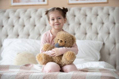 Pijama giymiş sevimli küçük bir kız evde oyuncak tavşanına sarılıyor, mutlu çocukluk konsepti, kapalı alanda.