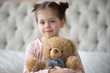 Pijama giymiş sevimli küçük bir kız evde oyuncak tavşanına sarılıyor, mutlu çocukluk konsepti, kapalı alanda.