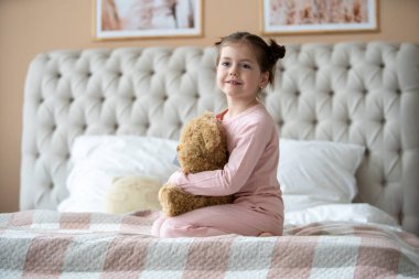 Pijama giymiş sevimli küçük bir kız evde oyuncak tavşanına sarılıyor, mutlu çocukluk konsepti, kapalı alanda.