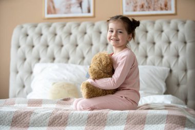 Pijama giymiş sevimli küçük bir kız evde oyuncak tavşanına sarılıyor, mutlu çocukluk konsepti, kapalı alanda.