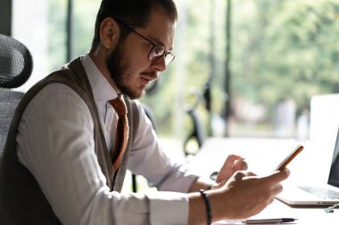 İşle meşgul. Ofiste oturan akıllı telefonu tutan gülümseyen bir işadamı. Cep telefonu uygulamaları kullanan orta yaşlı bir yönetici. Dijital teknoloji uygulamaları ve iş geliştirme çözümleri