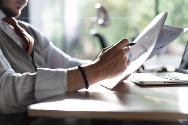 Businessman hands holding pen for working with stack of paper files, searching information, business report papers and piles of unfinished documents in modern office