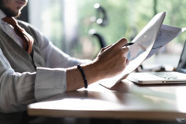 Businessman hands holding pen for working with stack of paper files, searching information, business report papers and piles of unfinished documents in modern office