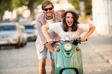 Kasabada scooter süren gülen bir çift. Motosiklet süren bir adam. Macera ve tatil kavramı