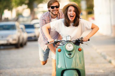 Kasabada scooter süren gülen bir çift. Motosiklet süren bir adam. Macera ve tatil kavramı
