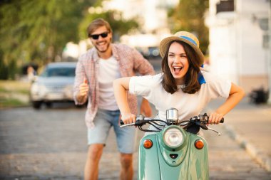 Kasabada scooter süren gülen bir çift. Motosiklet süren bir adam. Macera ve tatil kavramı