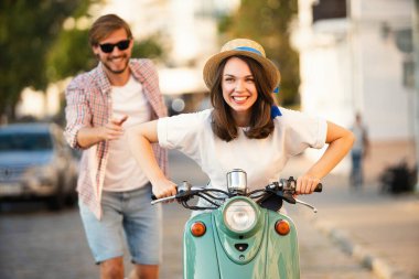 Kasabada scooter süren gülen bir çift. Motosiklet süren bir adam. Macera ve tatil kavramı
