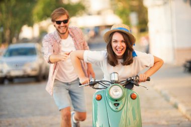 Kasabada scooter süren gülen bir çift. Motosiklet süren bir adam. Macera ve tatil kavramı