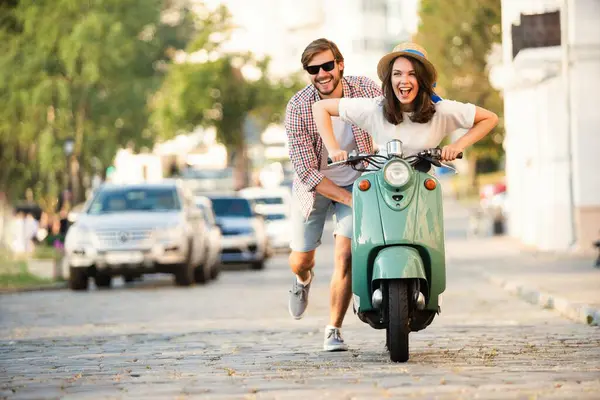 Kasabada scooter süren gülen bir çift. Motosiklet süren bir adam. Macera ve tatil kavramı