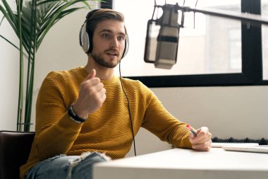 Adam podcaster etkili blogcu gülümseyerek stüdyoda kulaklık, dizüstü bilgisayar ve kulaklık kullanarak canlı yayın yapıyor. Erkek radyo sunucusu podcast veya röportaj yapıyor