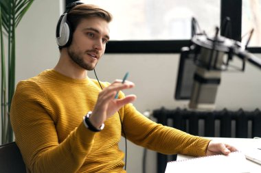 Adam podcaster etkili blogcu gülümseyerek stüdyoda kulaklık, dizüstü bilgisayar ve kulaklık kullanarak canlı yayın yapıyor. Erkek radyo sunucusu podcast veya röportaj yapıyor