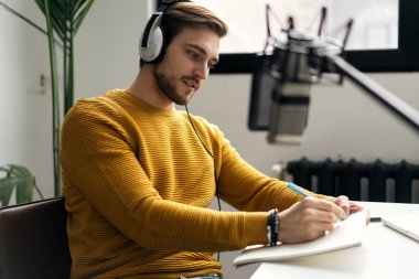 Adam podcaster etkili blogcu gülümseyerek stüdyoda kulaklık, dizüstü bilgisayar ve kulaklık kullanarak canlı yayın yapıyor. Erkek radyo sunucusu podcast veya röportaj yapıyor