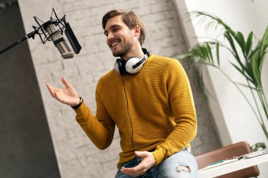 Adam podcaster etkili blogcu gülümseyerek stüdyoda kulaklık, dizüstü bilgisayar ve kulaklık kullanarak canlı yayın yapıyor. Erkek radyo sunucusu podcast veya röportaj yapıyor