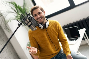 Adam podcaster etkili blogcu gülümseyerek stüdyoda kulaklık, dizüstü bilgisayar ve kulaklık kullanarak canlı yayın yapıyor. Erkek radyo sunucusu podcast veya röportaj yapıyor