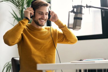 Adam podcaster etkili blogcu gülümseyerek stüdyoda kulaklık, dizüstü bilgisayar ve kulaklık kullanarak canlı yayın yapıyor. Erkek radyo sunucusu podcast veya röportaj yapıyor