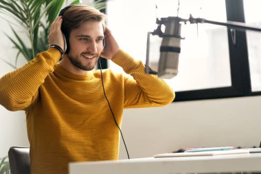 Adam podcaster etkili blogcu gülümseyerek stüdyoda kulaklık, dizüstü bilgisayar ve kulaklık kullanarak canlı yayın yapıyor. Erkek radyo sunucusu podcast veya röportaj yapıyor