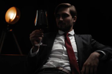 İş adamı dinleniyor. Karanlık bir odada bir bardak şarapla yakışıklı ve zarif bir adamın portresi.