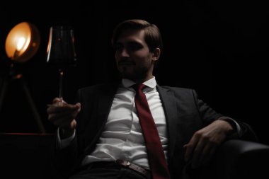 İş adamı dinleniyor. Karanlık bir odada bir bardak şarapla yakışıklı ve zarif bir adamın portresi.